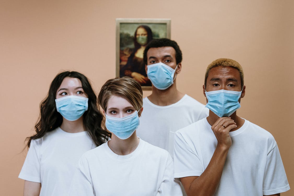 Empat orang anak muda mengenakan kaos putih dan masker medis di depan lukisan Monalisa yang memakai masker